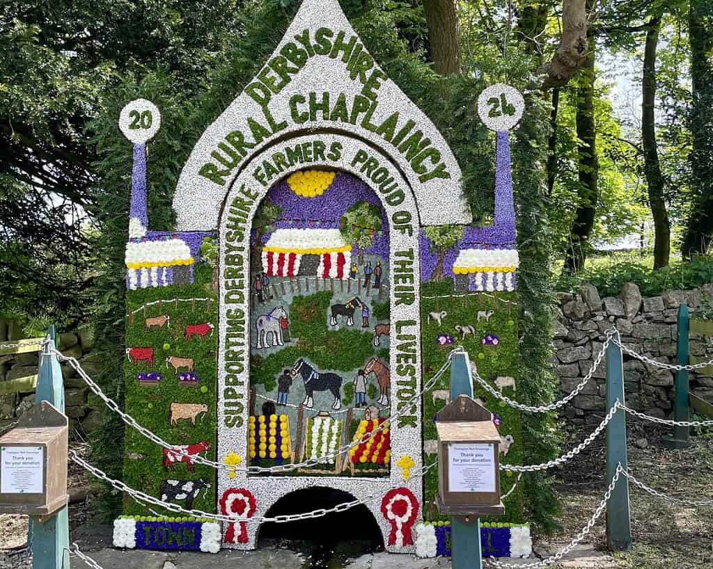 Een kleurrijk bloemstuk in de vorm van een kapel met de tekst "Derbyshire Rural Chaplaincy 2024". Er staan boerderijdieren en boeren op afgebeeld met de tekst "Taking it Easy-supporting Derbyshire farmers, proud of their livestock.