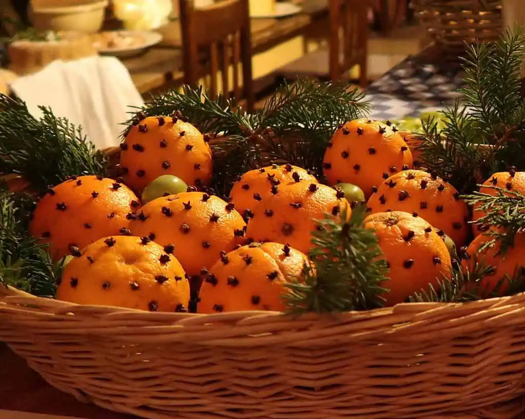 Een rieten mand gevuld met sinaasappels bezaaid met kruidnagels, versierd met dennentakken, staat op een tafel binnenshuis en brengt een feestelijke en geurige wintersfeer die doet denken aan Kent en Sussex.