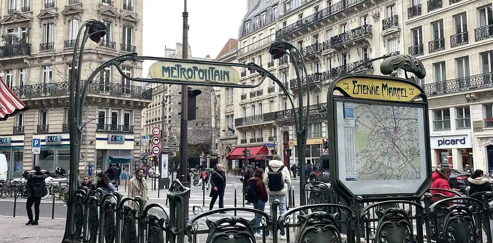 Art Nouveau Parijse metro-ingang op station Étienne Marcel, met versierde groene balustrades, een plattegrond en mensen die vlakbij lopen; klassieke Parijse gebouwen met balkons op de achtergrond.