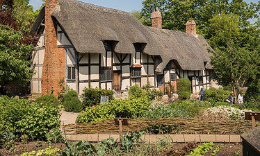 Een traditionele Engelse cottage met een rieten dak en vakwerkmuren, omringd door weelderige tuinen met groenten en bloemen, roept de charme op van het platteland van Shakespeare, allemaal onder een strakblauwe hemel.